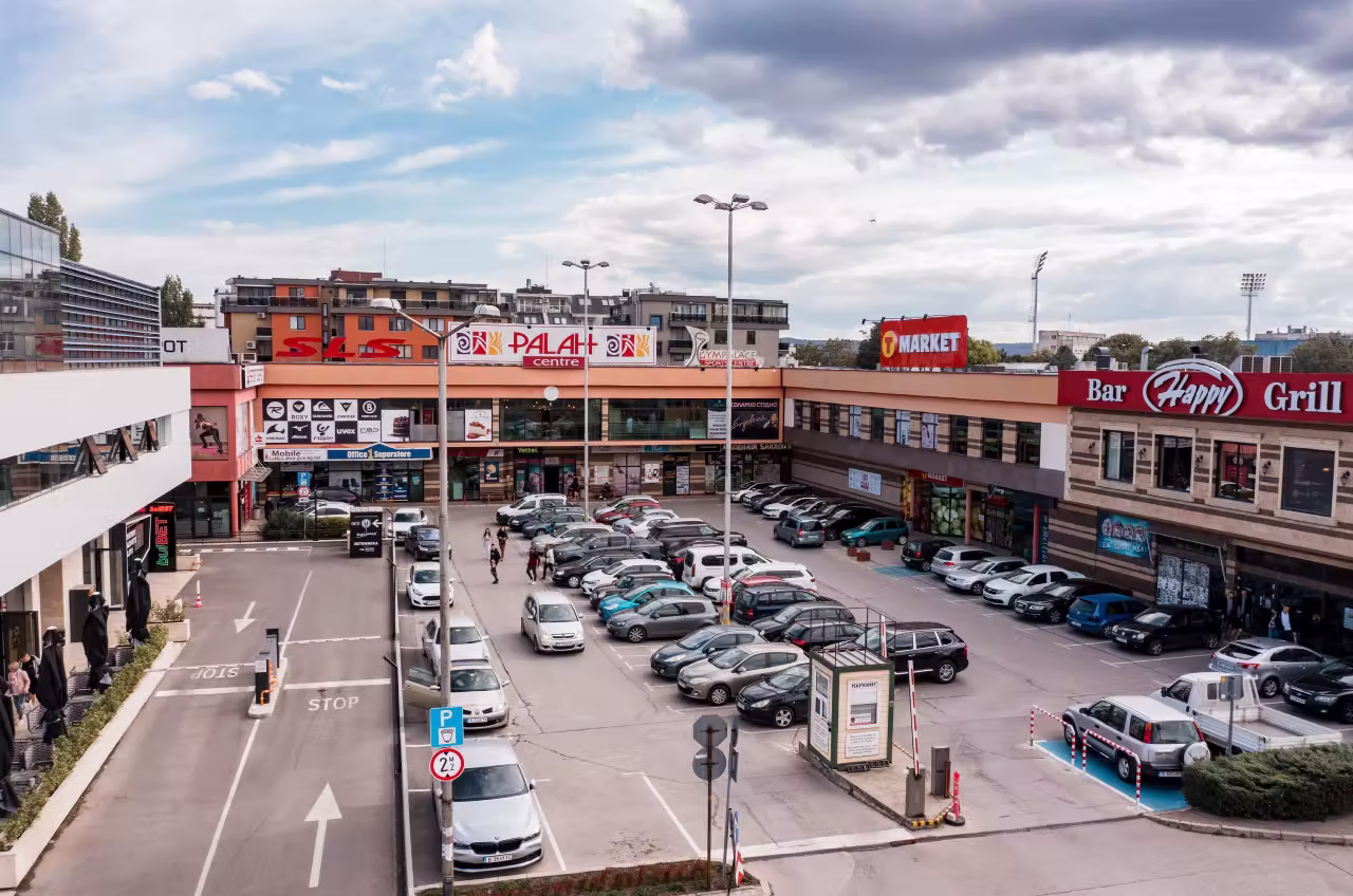 Паркинг на търговски център с коли и табели под облачно небе